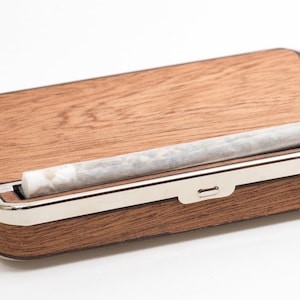 May include: A wooden box with a silver trim and a rolled cigarette inside. The box has a slot for holding the cigarette.