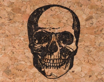 May include: A black and white skull illustration printed on a cork background.