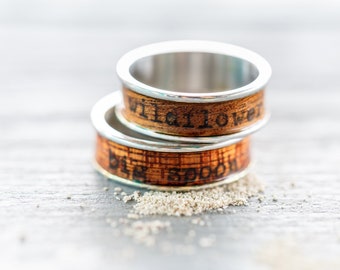 May include: Two wooden rings with silver bands. The top ring has the words "Wildflower" engraved on it. The bottom ring has the words "Big Spoon" engraved on it.