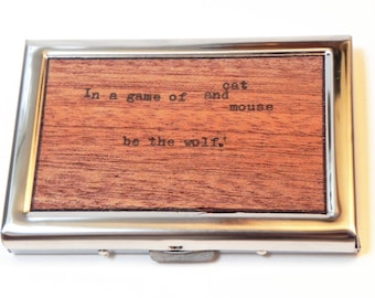 May include: A silver metal card holder with a wooden insert. The wood has a quote engraved on it that reads "In a game of cat and mouse be the wolf!"
