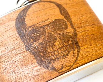 May include: A wooden flask with a skull design burned into the wood. The flask has a silver metal rim.