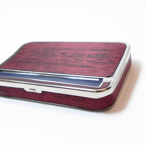 May include: A rectangular box with a burgundy wood-grain finish and a silver-colored metal trim. The box has a hinged lid and a blue fabric interior. The design is sleek and modern, suitable for storing small items.