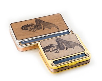 May include: Two wooden rolling trays with a mermaid design. The top tray is silver and the bottom tray is gold.