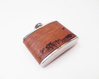 May include: A silver flask with a woodgrain design and a laser-etched image of a cityscape.