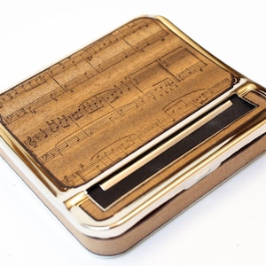 Op de afbeelding: Een bruine metalen roltafel met een muzieknootontwerp. De tafel heeft een ingebouwd rolmechanisme en een zilveren rand.