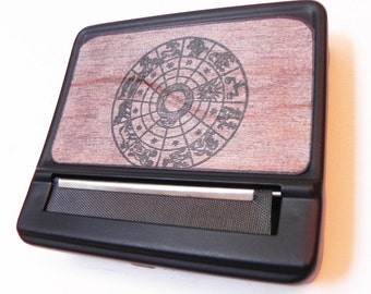 May include: A black rolling tobacco case with a wooden lid featuring a circular design of zodiac symbols. The case has a metal rolling tray.