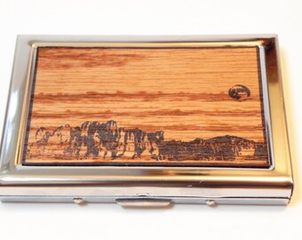May include: A silver metal card holder with a wood inlay featuring a black and white image of a mountain range and a moon.