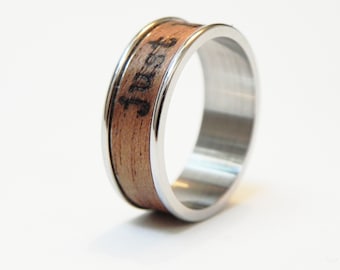 May include: A silver ring with a wooden inlay. The wood is a light brown color and has the word "Trust" burned into it.