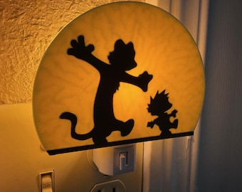 May include: A night light featuring a black silhouette of two cartoon characters on a yellow background. The night light is plugged into a wall outlet and has an on/off switch.