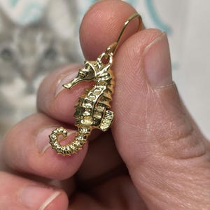 May include: Gold-toned seahorse dangle earrings. The seahorse is detailed with textured scales and a curled tail.