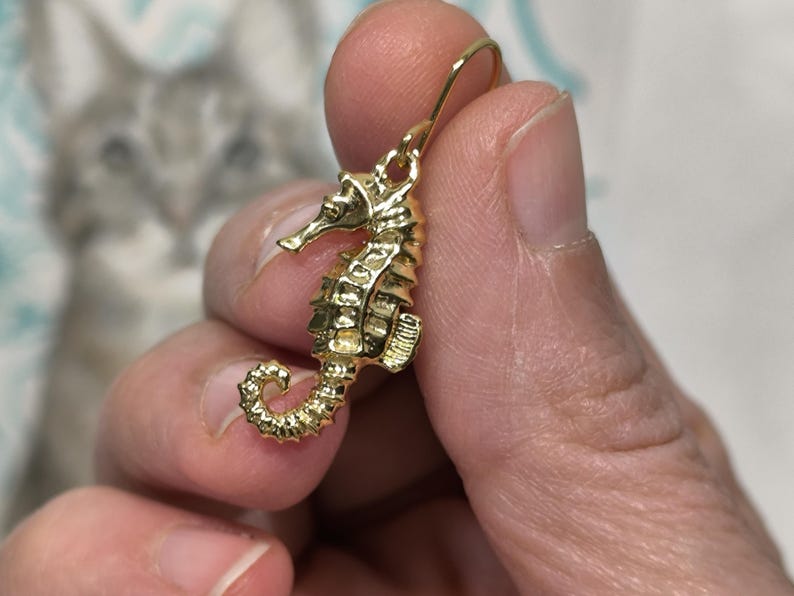 May include: Gold-toned seahorse dangle earrings. The seahorse is detailed with textured scales and a curled tail.