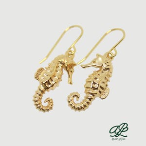 May include: A pair of gold-tone earrings featuring a detailed seahorse design. The earrings are made of metal and have a dangling style.