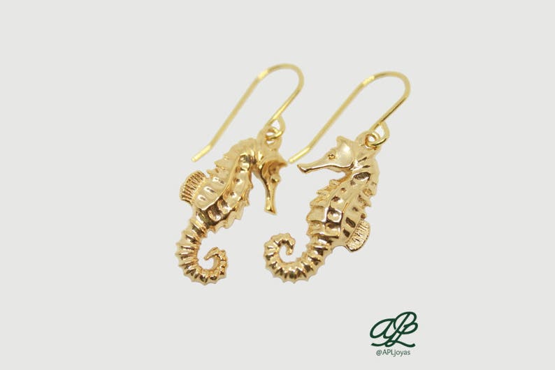 May include: A pair of gold-tone earrings featuring a detailed seahorse design. The earrings are made of metal and have a dangling style.