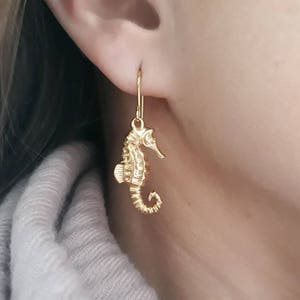 May include: Gold-toned seahorse dangle earrings. The seahorse is detailed and has a curled tail.