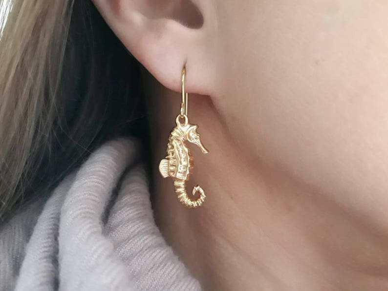 May include: Gold-toned seahorse dangle earrings. The seahorse is detailed and has a curled tail.