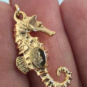 May include: Gold-tone seahorse pendant with a detailed design and a small logo on the side.