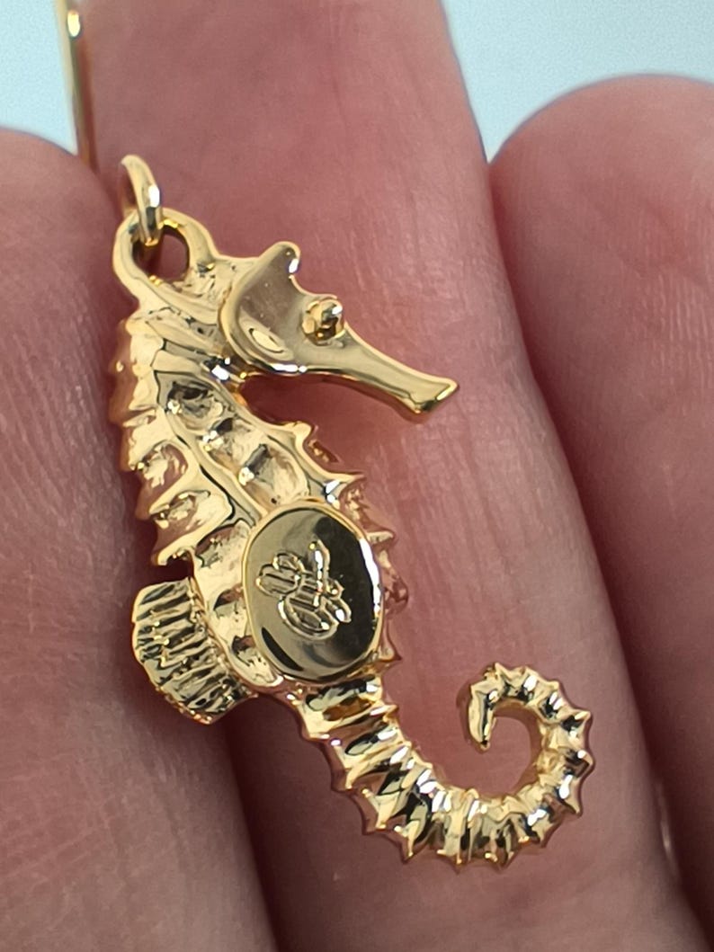 May include: Gold-tone seahorse pendant with a detailed design and a small logo on the side.