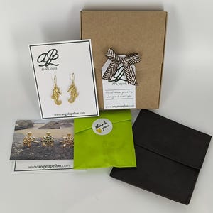 May include: A brown cardboard box with a green gift bag and a thank you sticker. The box has a tag that says "AP Joyas Handmade jewelry designed for you www.angelapellon.com". The gift bag has a sticker that says "Thank you".