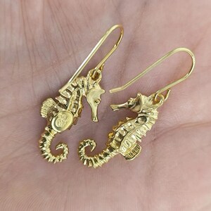 May include: A pair of gold-tone seahorse earrings with a dangling design. The earrings are made of metal and have a polished finish.