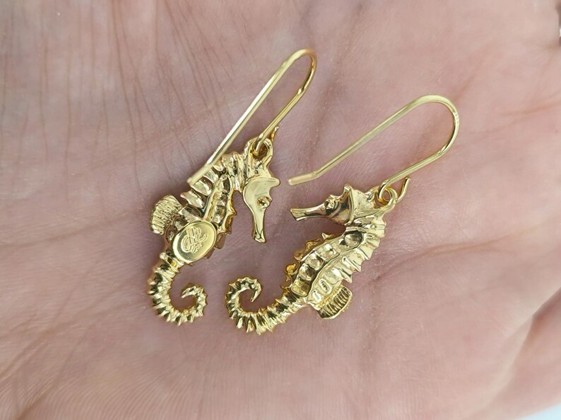 May include: A pair of gold-tone seahorse earrings with a dangling design. The earrings are made of metal and have a polished finish.