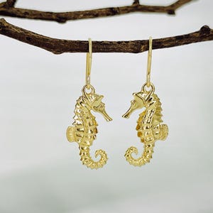 May include: Gold-tone seahorse earrings with a detailed design. The earrings are hanging from a branch.
