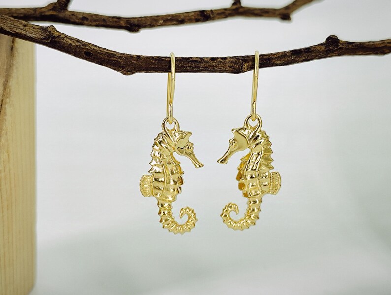 May include: Gold-tone seahorse earrings with a detailed design. The earrings are hanging from a branch.