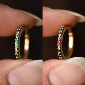 Peut inclure: Deux créoles en or ornées de petites pierres précieuses. La boucle de gauche présente des pierres noires avec deux pierres vertes au centre. La boucle de droite présente des pierres noires avec deux pierres roses au centre. Finition dorée.