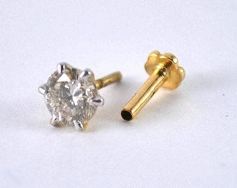 May include: Two pieces of jewelry: a gold-colored stud with a flower-shaped top and a diamond stud with a six-prong setting. The diamond is clear and the metal is silver-colored. The studs are on a white background.