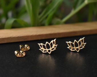 Puede incluir: Pendientes de botón con forma de flor de loto dorada. Los pendientes se muestran con sus respaldos sobre una superficie negra. El diseño de la flor de loto es detallado y delicado, con múltiples pétalos. Una joya.