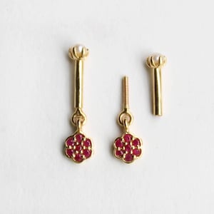 May include: A gold body jewellery piece featuring a long post topped with a small white pearl, and a dangling flower-shaped charm set with seven small red rubies. Beside it, a separate gold post with a pearl top and a matching ruby flower charm.