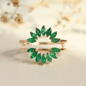 Può includere: Un anello d'oro con un design a doppia fascia, ornato da vivaci smeraldi verdi. Gli smeraldi sono taglio marquise e disposti a raggiera, creando un gioiello elegante e di grande effetto.
