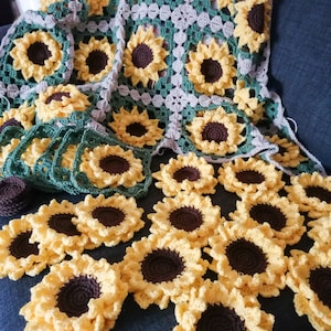 Puede incluir: Una manta de ganchillo con un dise&ntilde;o de girasol. La manta est&aacute; hecha de hilo verde, marr&oacute;n y beige. Hay muchos motivos de girasol individuales en primer plano.