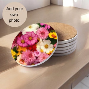 May include: A set of six round coasters with a floral design. The coasters feature a variety of pink, white, and yellow flowers. The coasters are made of a white ceramic material and have a cork backing.