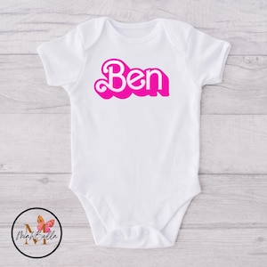 May include: White baby onesie with a pink retro-style font spelling "Ben".