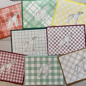 Pode incluir: Oito cartões com diferentes padrões de xadrez em vermelho, verde, amarelo e marrom. Cada cartão apresenta uma ilustração em preto e branco de um cão.