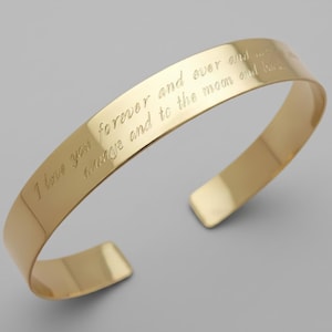 May include: A gold-colored cuff bracelet with the engraved text "I love you forever and ever always and to the moon and back." The bracelet has a smooth, polished finish and an open design.