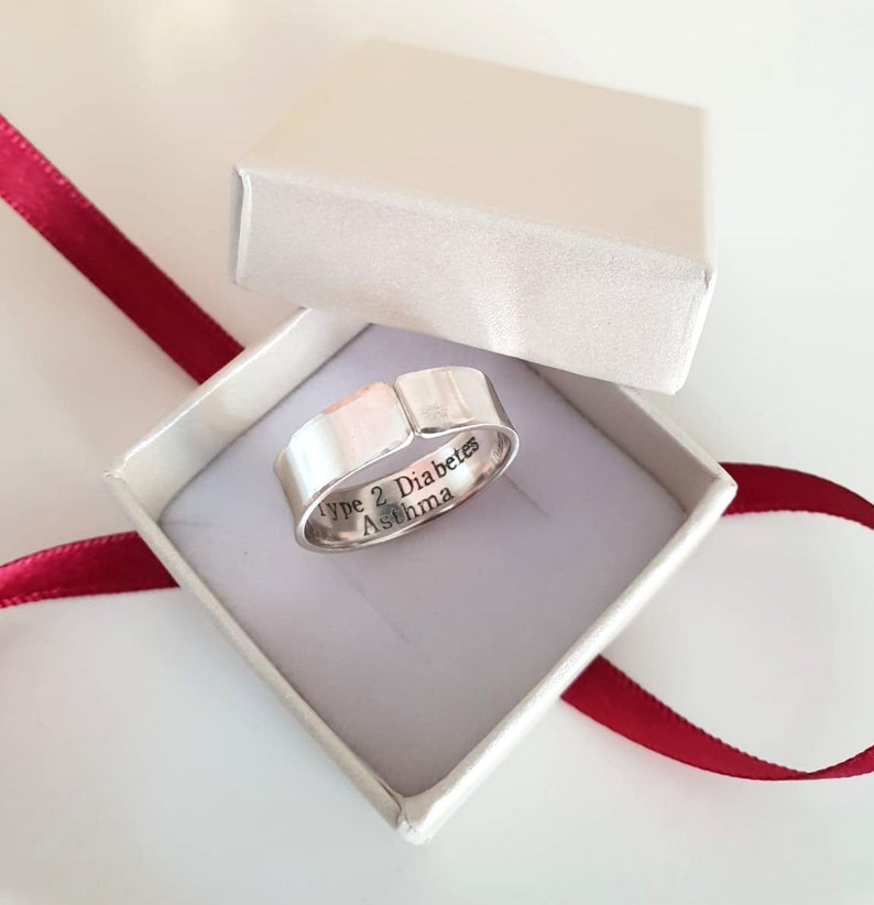 May include: A silver ring with the words "Type 2 Diabetes Asthma" engraved on the inside of the band. The ring is in a white box with a red ribbon.