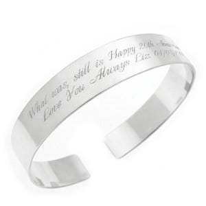 May include: A silver cuff bracelet with engraved text. The text reads "What was, still is Happy 20th Anniversary Love You Always Liz. 04/03/04". The bracelet has a polished finish and an open design.