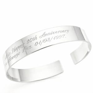 May include: A polished silver cuff bracelet with engraved text. The text reads "All is Happy 20th Anniversary I'm Always Liz. 01/03/1997." The bracelet has a simple, open design.