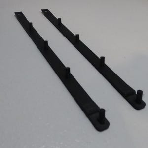 Può includere: Due pezzi di plastica neri, allungati, con più perni verticali. I pezzi sono posizionati in diagonale su uno sfondo bianco. I perni sono distanziati lungo i pezzi.