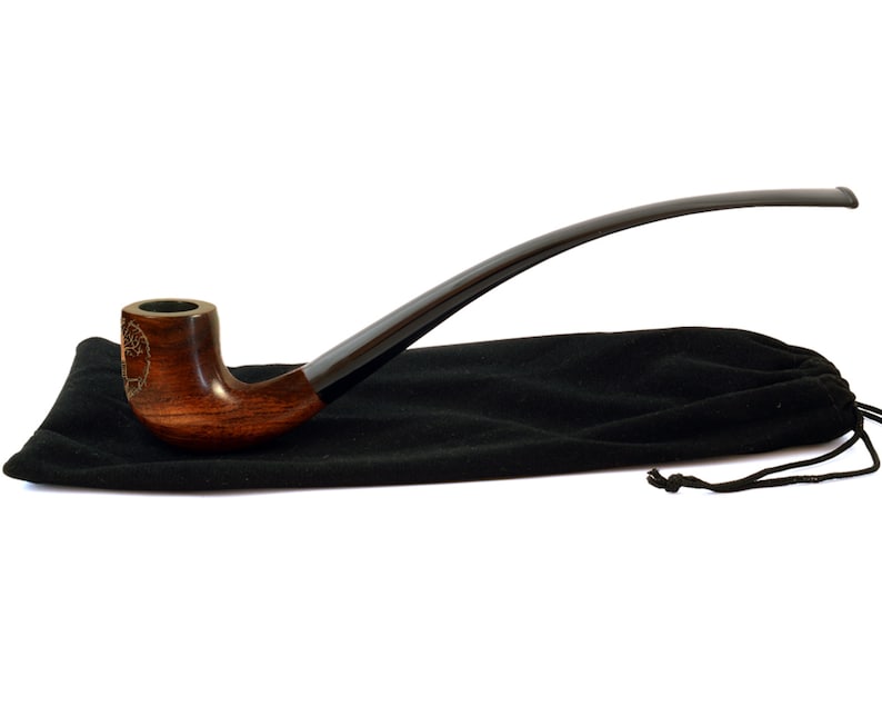 May include: A brown wooden smoking pipe with a black stem and a tree design on the bowl. The pipe is resting on a black velvet pouch.