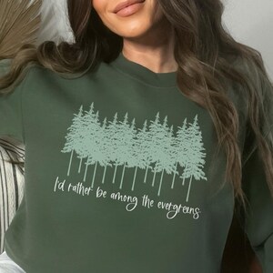 May include: A green sweatshirt with a graphic of a row of evergreen trees and the text "I'd rather be among the evergreens".
