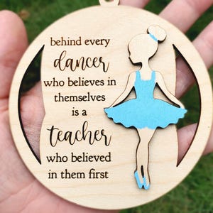 May include: Wooden round ornament with a cutout design. The ornament features a ballerina in a blue tutu and the text: "behind every dancer who believes in themselves is a teacher who believed in them first."