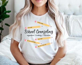 May include: White crew neck t-shirt featuring the words "School Counselling" and motivational phrases on yellow pencil graphics. Phrases include "Kindness matters" and "You can do hard things".