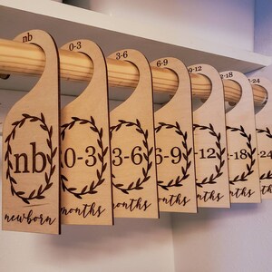 Puede incluir: Separadores de armario de madera para ropa de bebé, con indicaciones de edad de recién nacido a 24 meses. Cada separador tiene un diseño de corona decorativa y cuelga de una barra de madera. Medidas en meses.