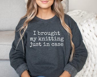 May include: A dark charcoal gray crewneck sweatshirt featuring the white text "I brought my knitting just in case" printed across the chest. The garment has long sleeves with ribbed cuffs and a ribbed neckline, providing a standard fit.