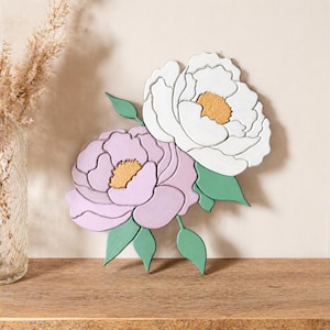 May include: Wooden floral wall art featuring two peony flowers. One flower is white with a gold center, and the other is lavender with a gold center. Green leaves accent the flowers, creating a decorative piece for home decor.