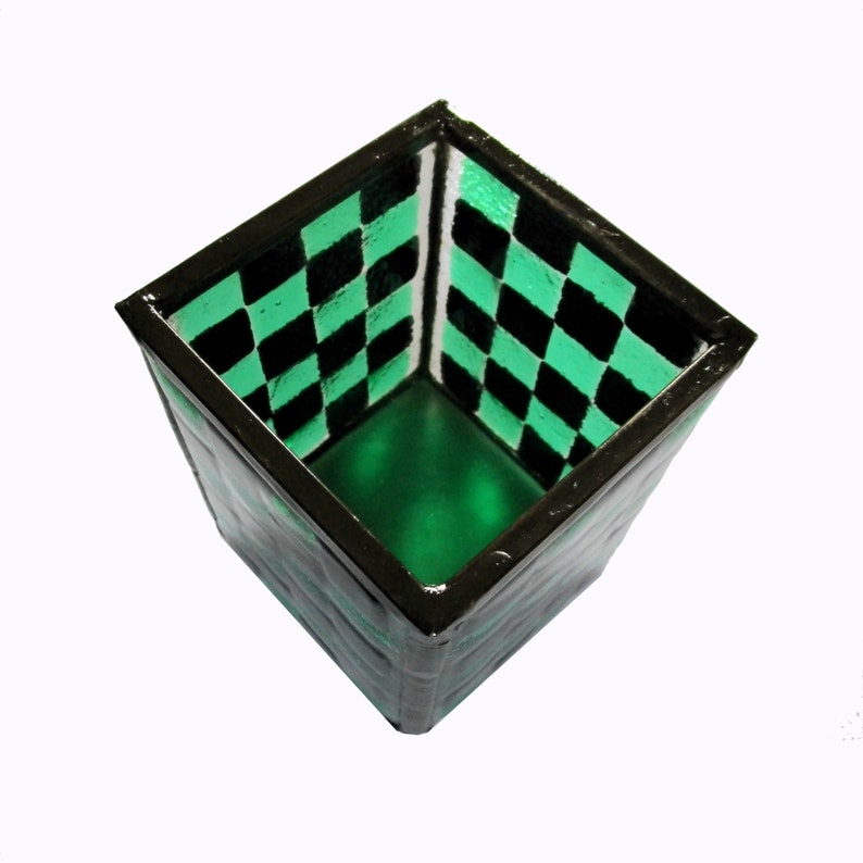 May include: A square green and black checkerboard patterned glass container with a black rim.