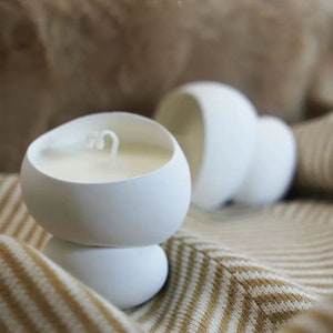 May include: Two white ceramic candle holders shaped like mushrooms. The candle holders are on a brown and white striped surface.