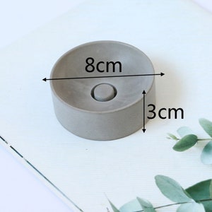 May include: A gray concrete ring dish with a diameter of 8 inches and a height of 3 inches. The dish has a small indentation in the center.
